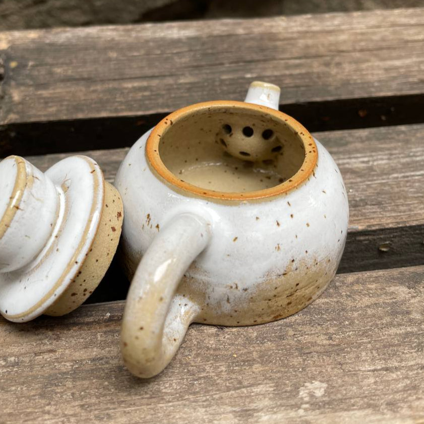 White ceramic teapot with brown interior on a wooden surface