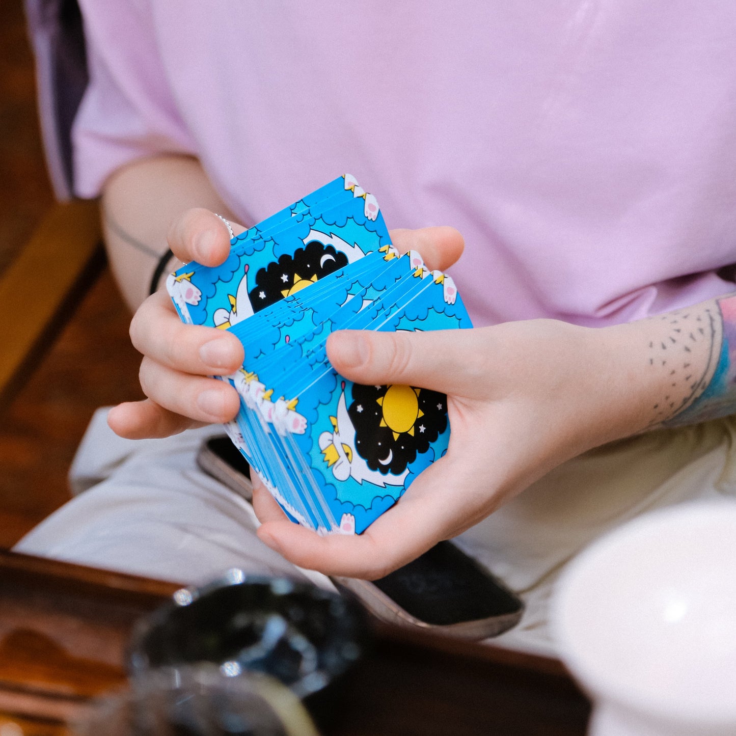 Person holding a blue card with cartoon designs, sitting at a table.