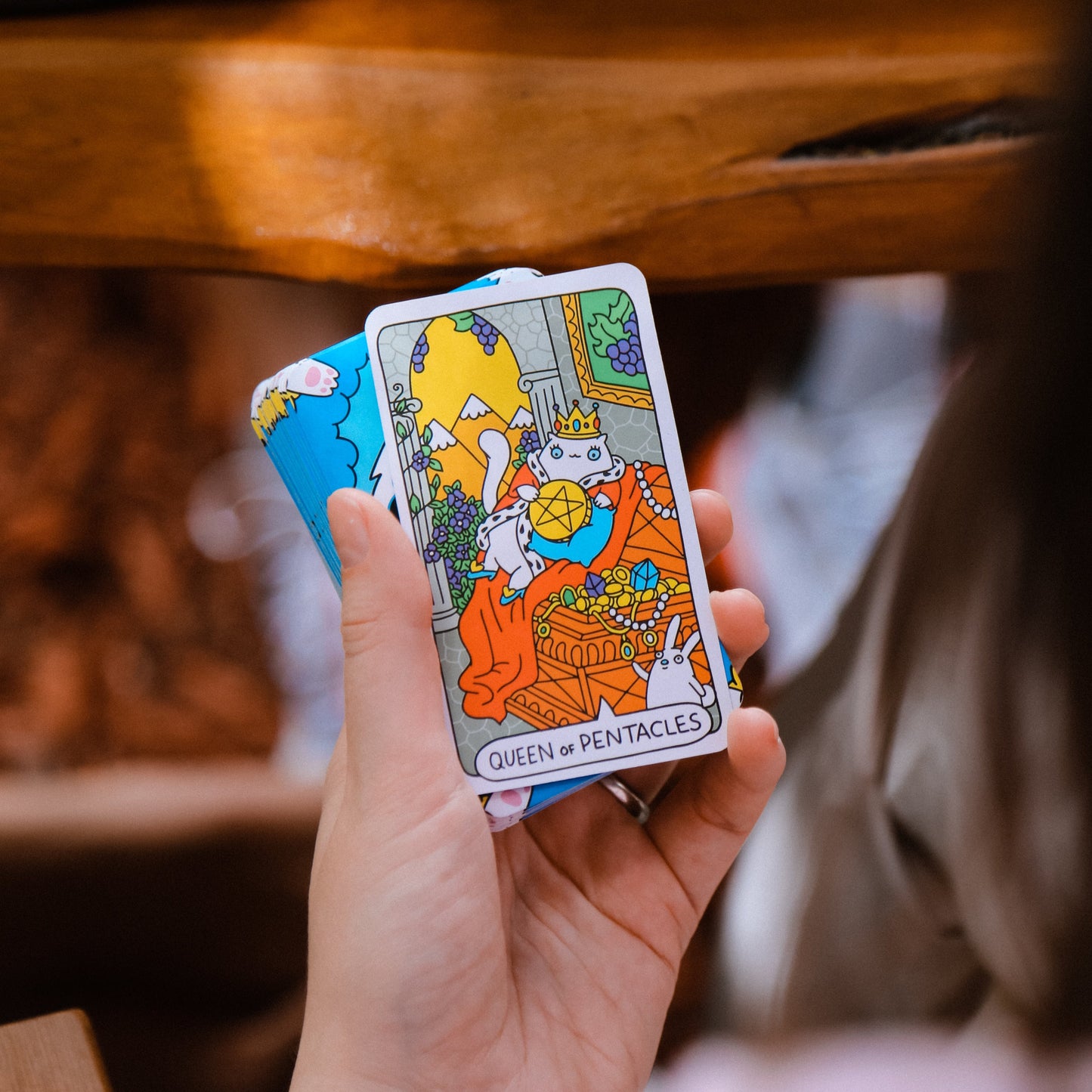 Hand holding a tarot card titled 'Queen of Pentacles' with a blurred background