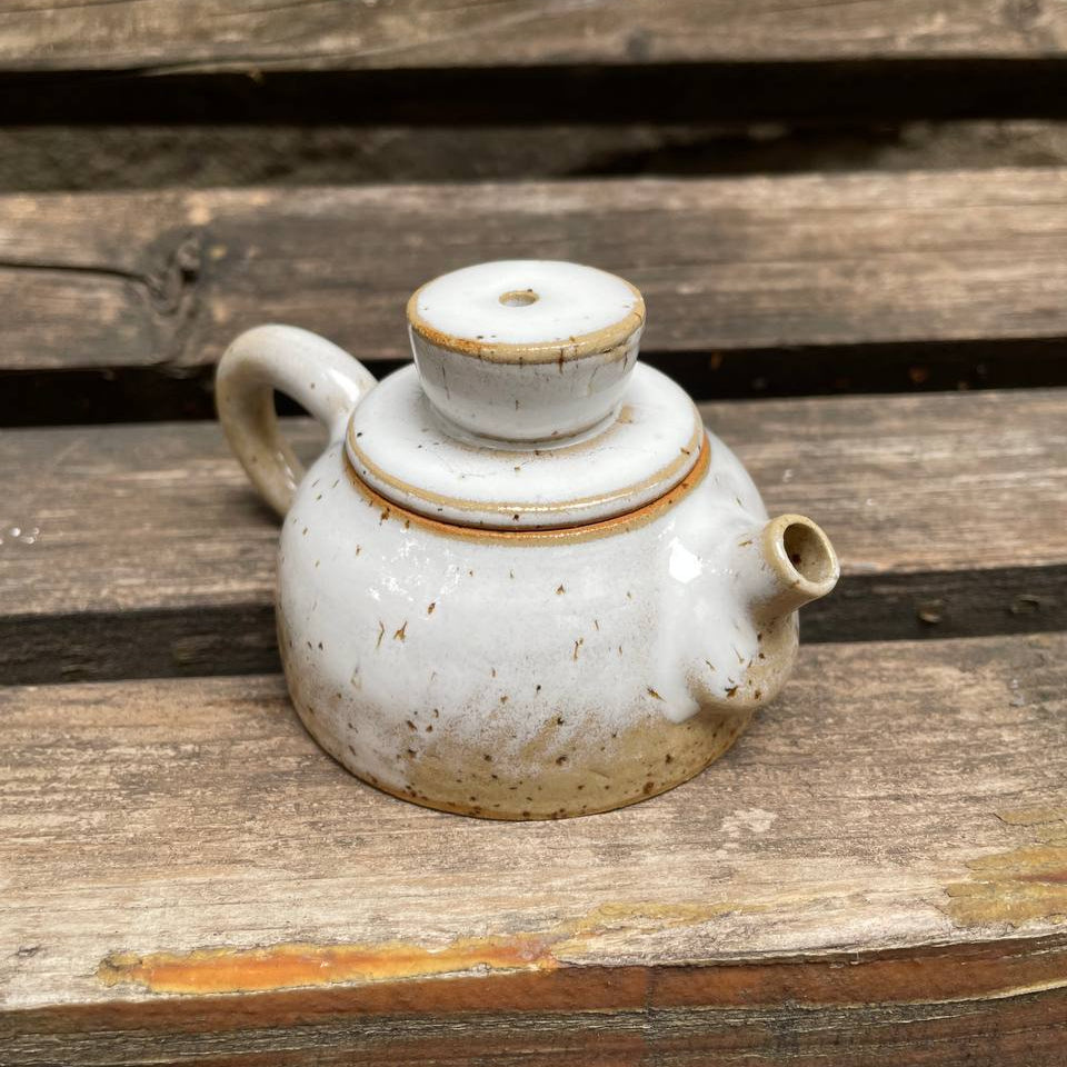 White ceramic teapot with brown speckles on a wooden surface