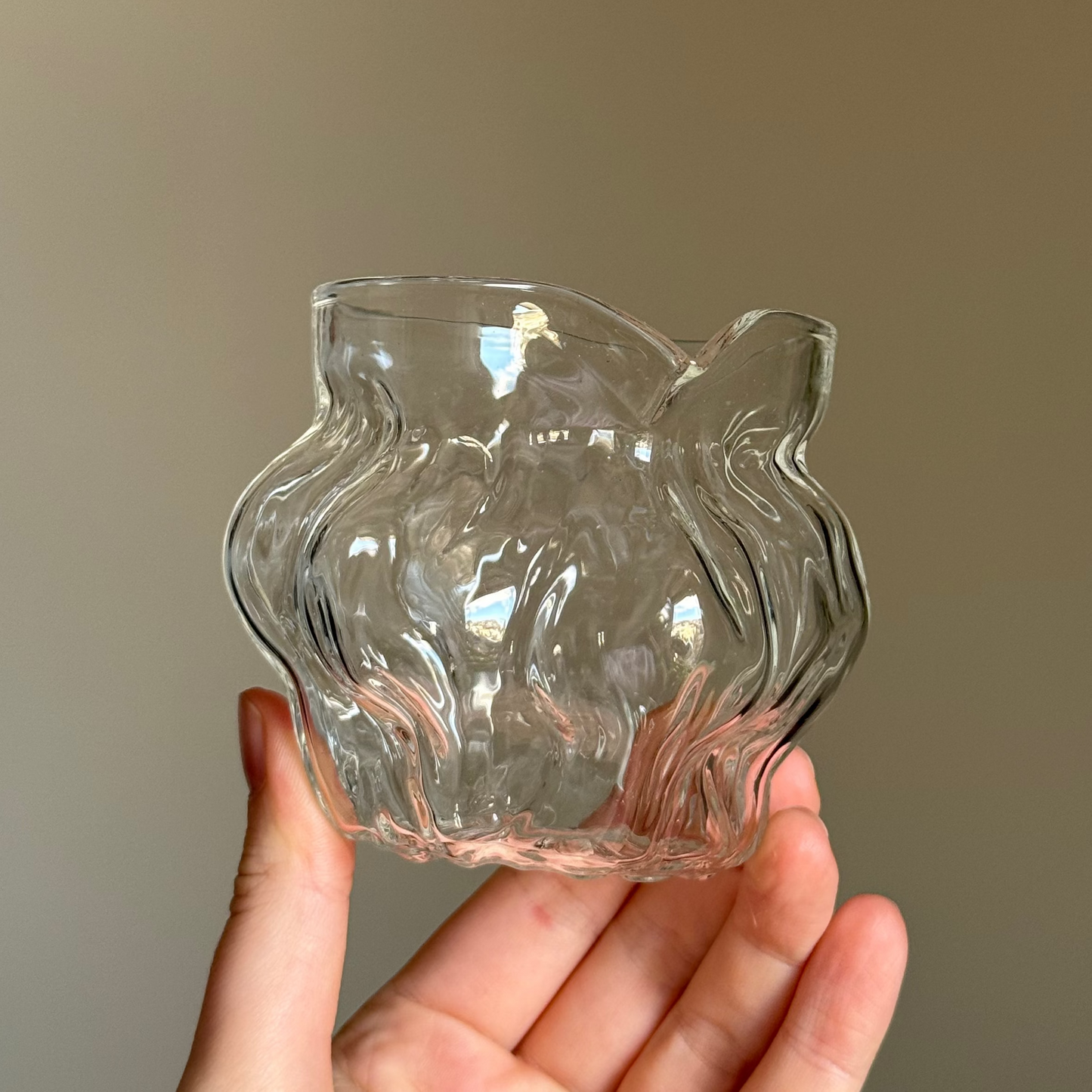 Clear glass candle holder shaped like a lion's head held in a hand against a neutral background